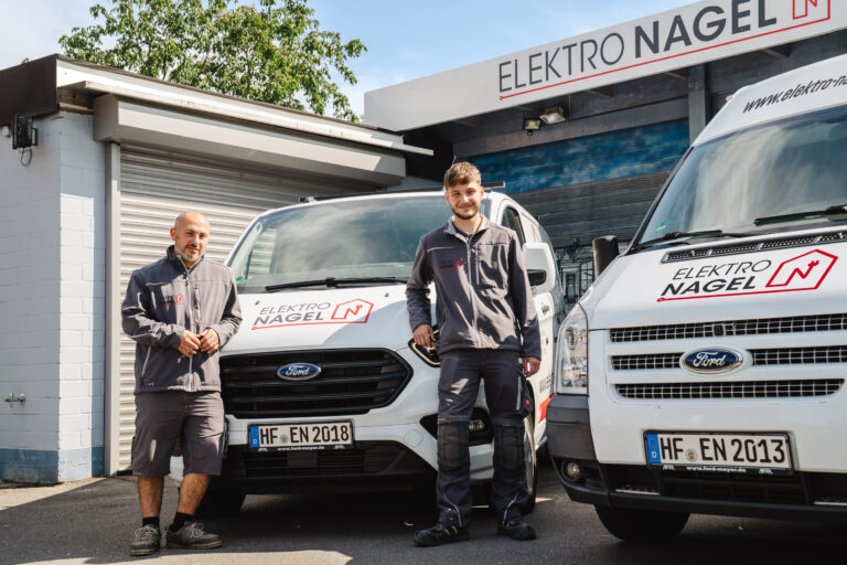 Zwei Personen stehen vor einem weißen Fahrzeug. Die Personen sind als Handwerker gekleidet, das Fahrzeug trägt das Logo "Elektro Nagel".