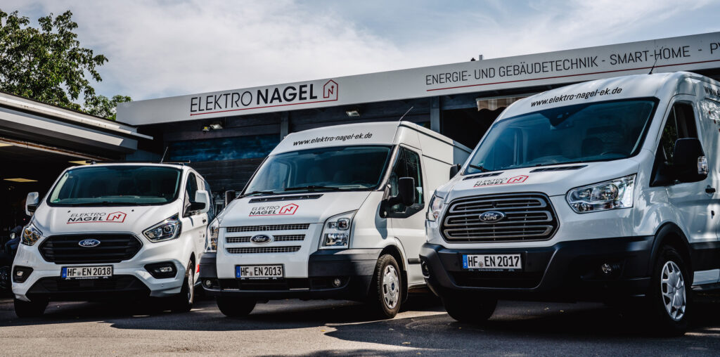 Drei weiße Fahrzeuge, die jeweils mit dem Firmenlogo "Elektro Nagel" beschriftet sind, stehen vor dem Firmengebäude.